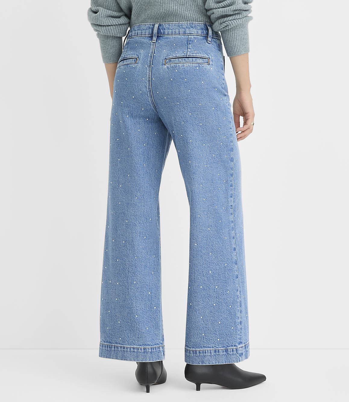 A person wearing light-wash wide-leg jeans with scattered rhinestones stands against a plain white background.