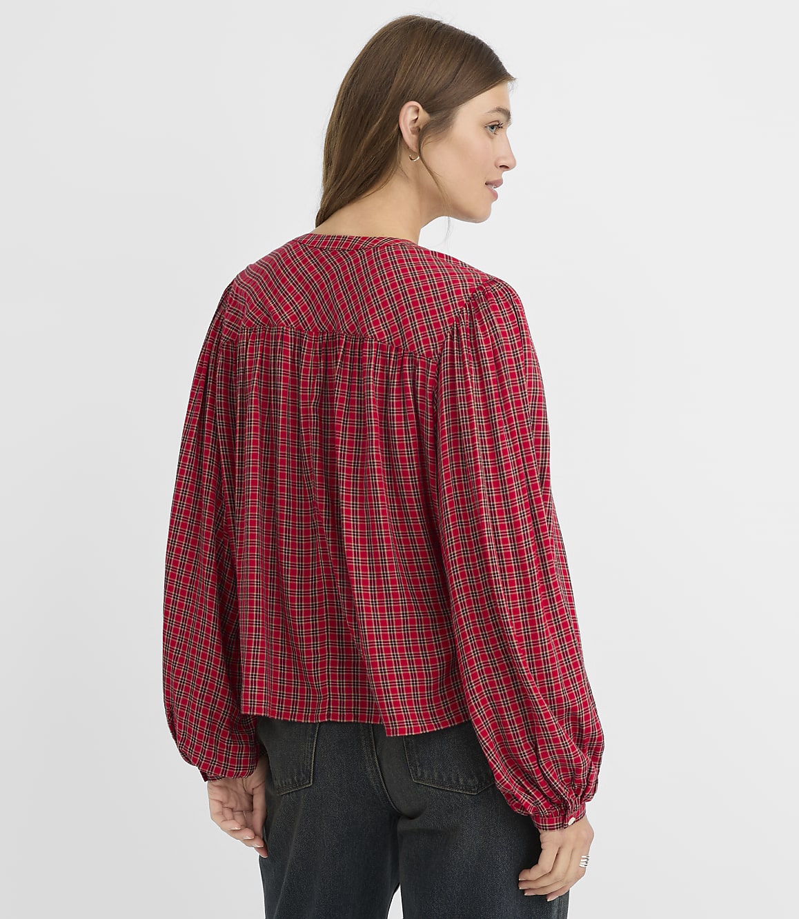 A woman in a red plaid blouse stands against a plain white background.