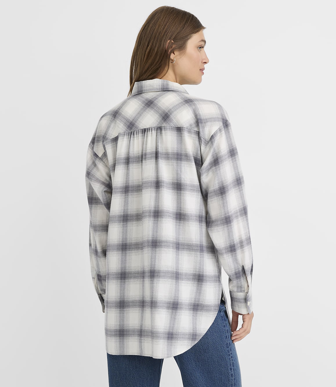 A woman in a grey and white plaid shirt stands against a plain white background.