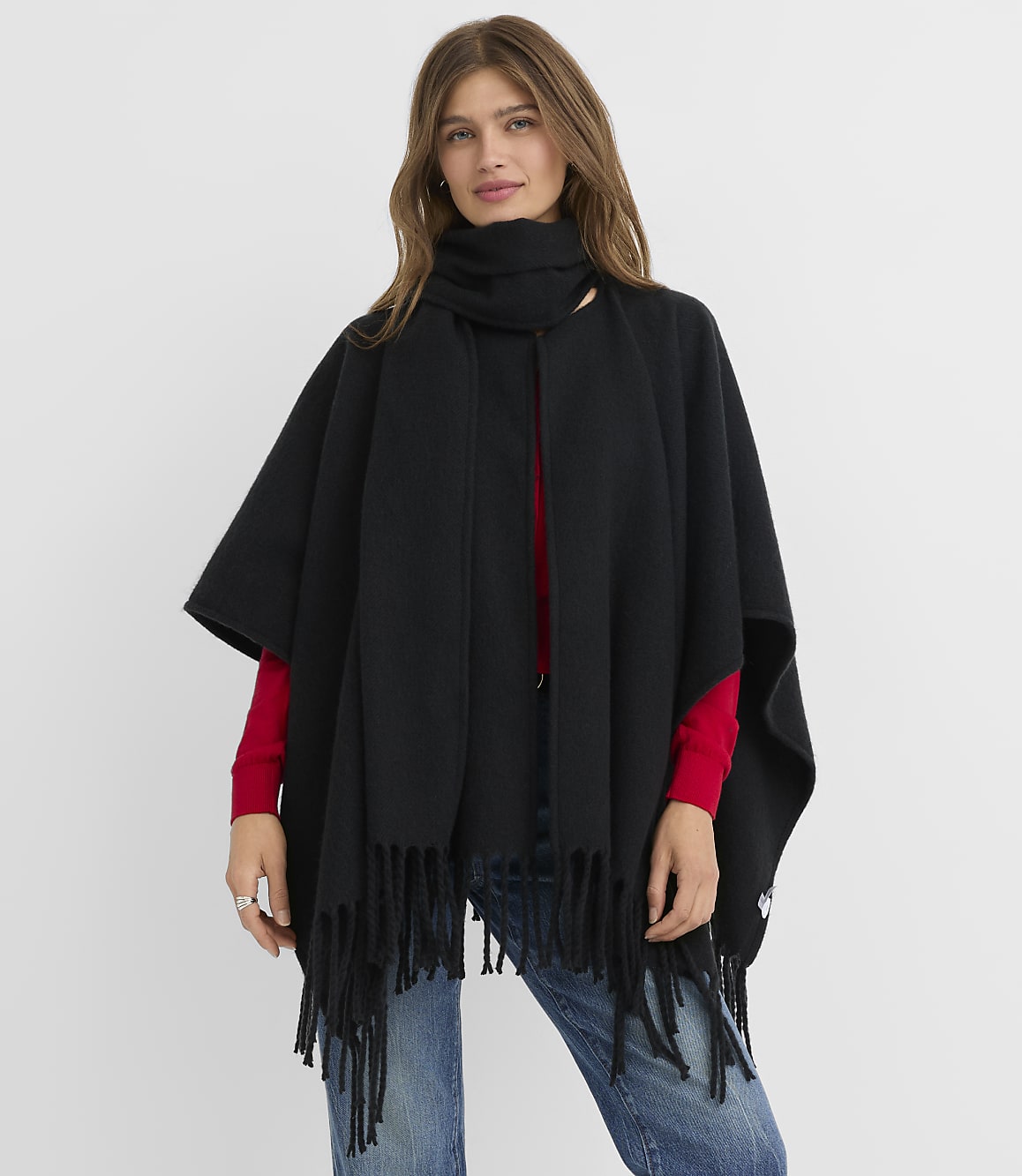 A woman in a black fringed poncho and scarf stands against a plain white background.