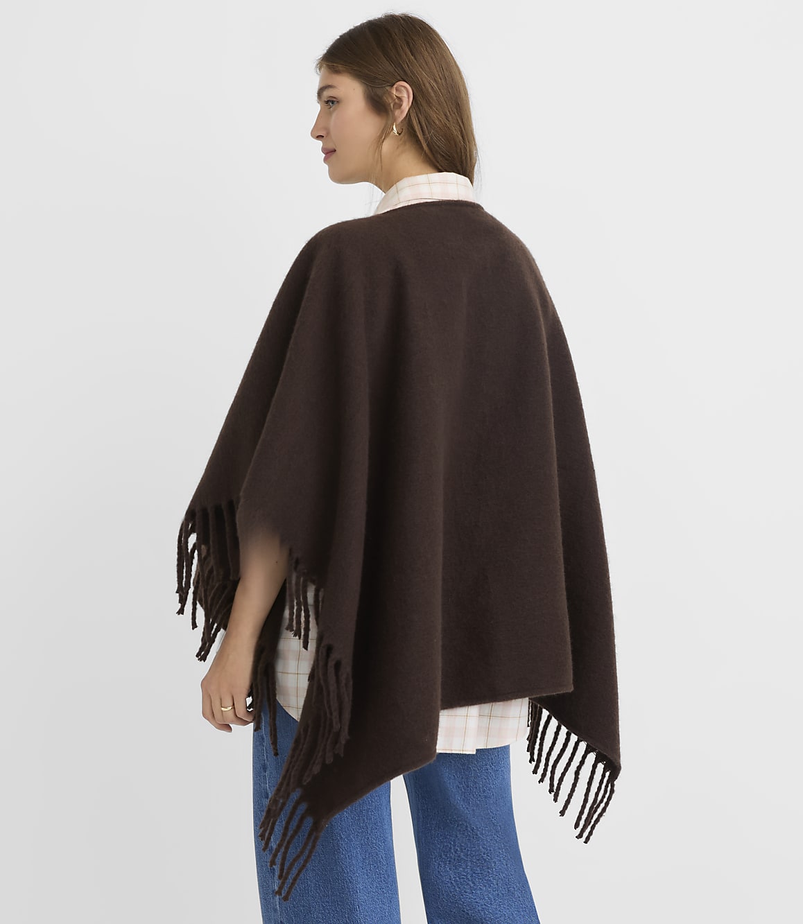 A woman in a brown fringed poncho and jeans stands against a plain white background.