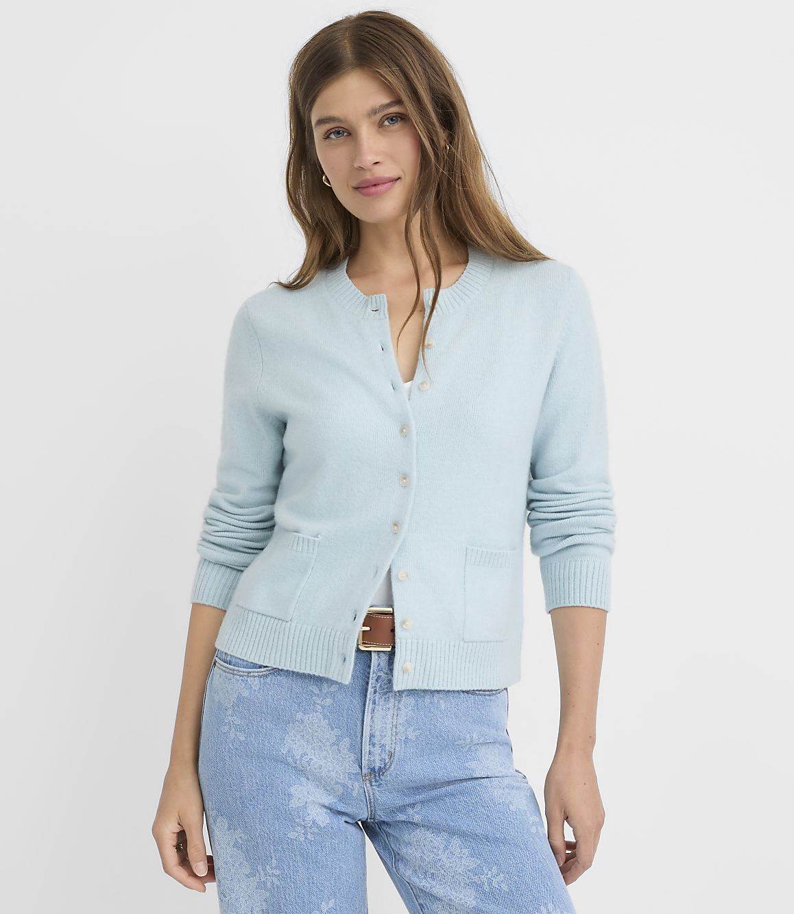 A woman in a light blue cardigan and jeans stands against a plain white background.