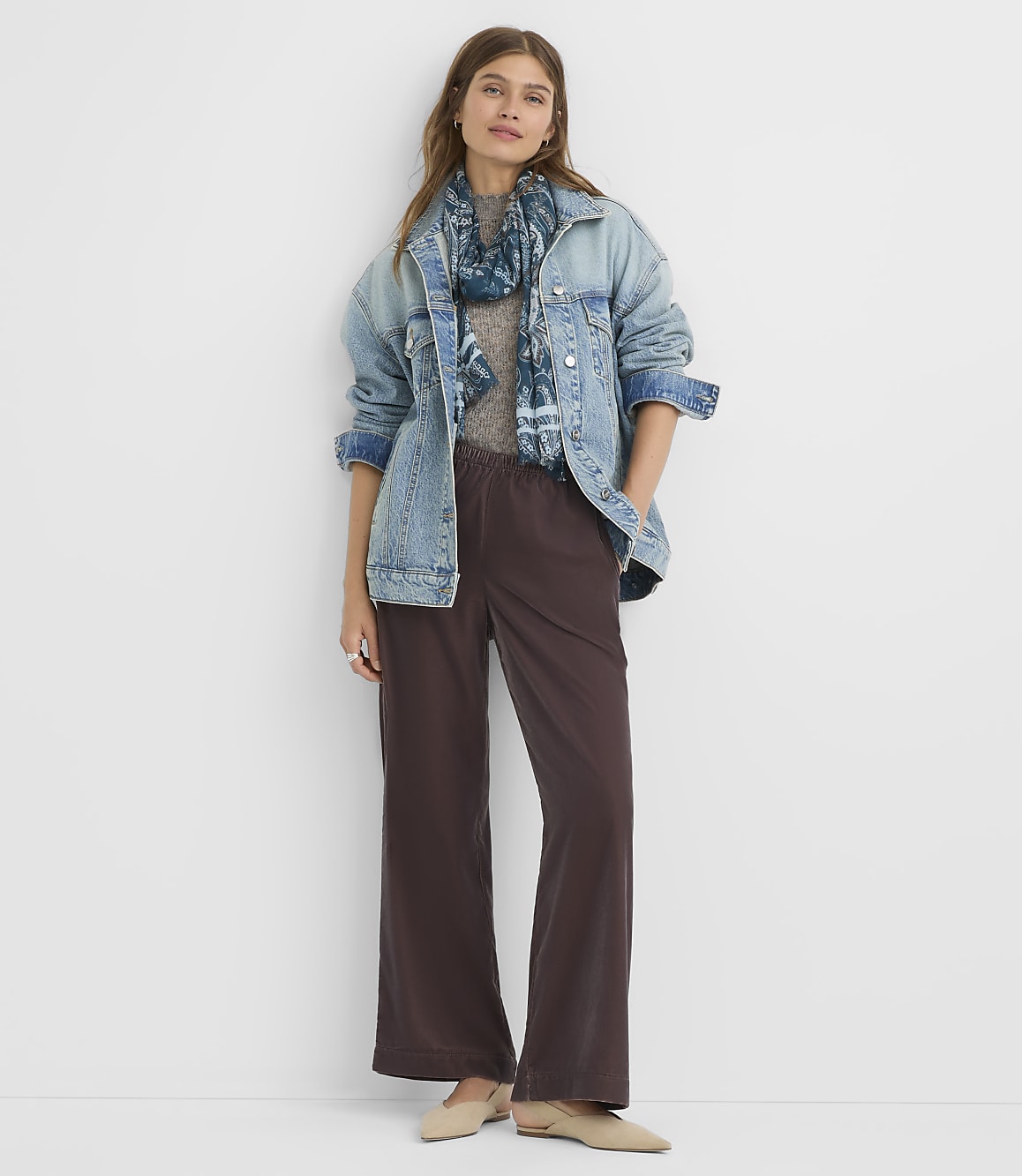 A woman in a denim jacket and wide-leg pants stands against a plain white background.