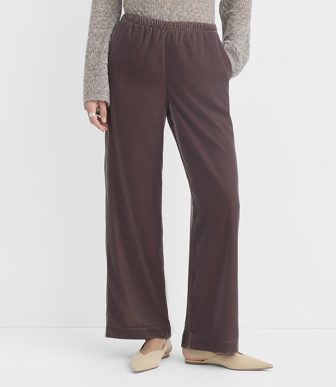 A person wearing brown wide-leg pants and a grey sweater stands on a white background.