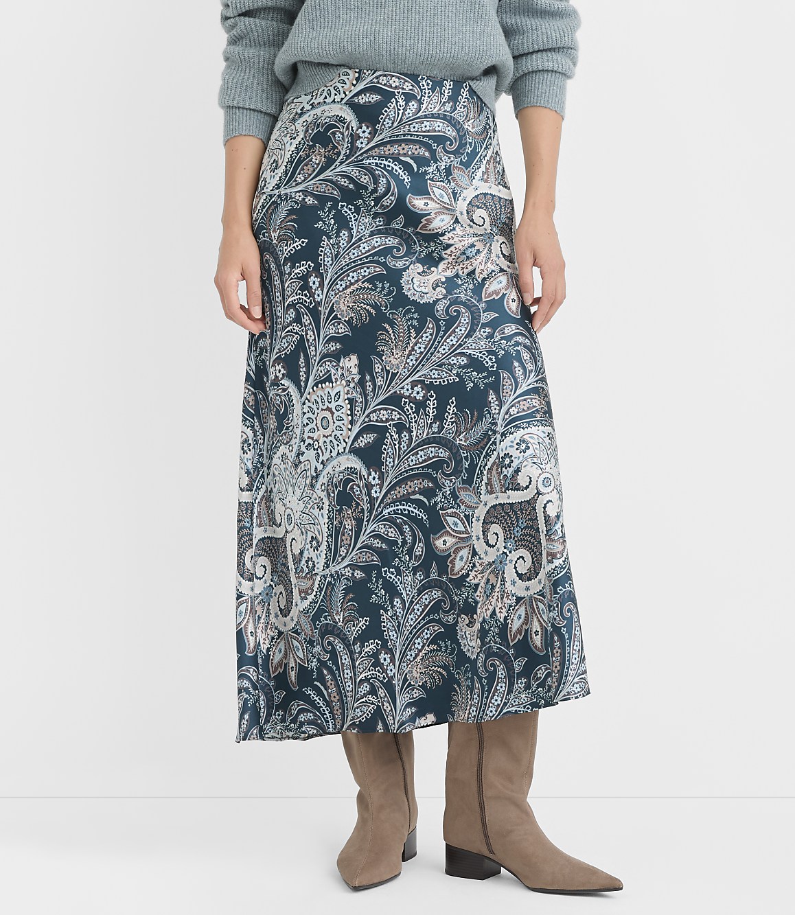 A woman in a teal paisley skirt and taupe boots stands against a plain white background.