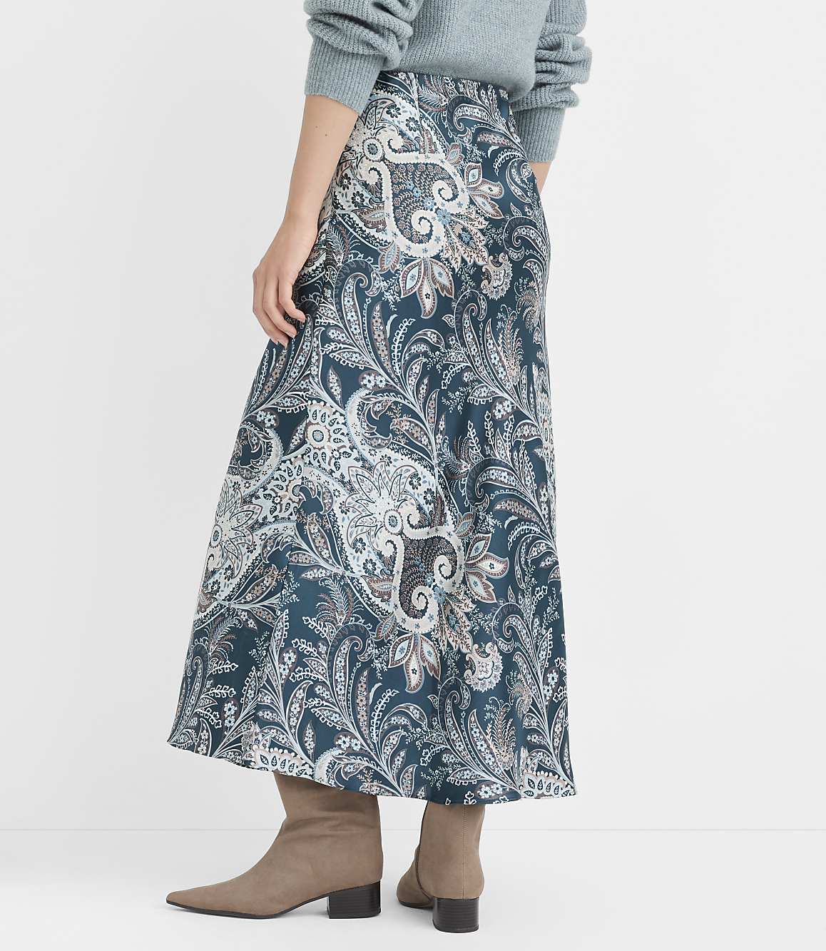 A woman in a teal paisley skirt and grey boots stands against a plain grey background.