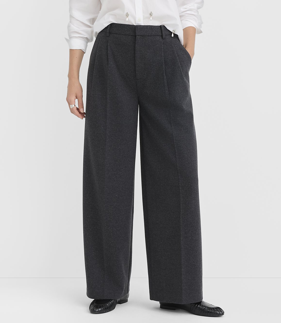 A person stands in dark grey wide-leg trousers and a white shirt against a plain white background.