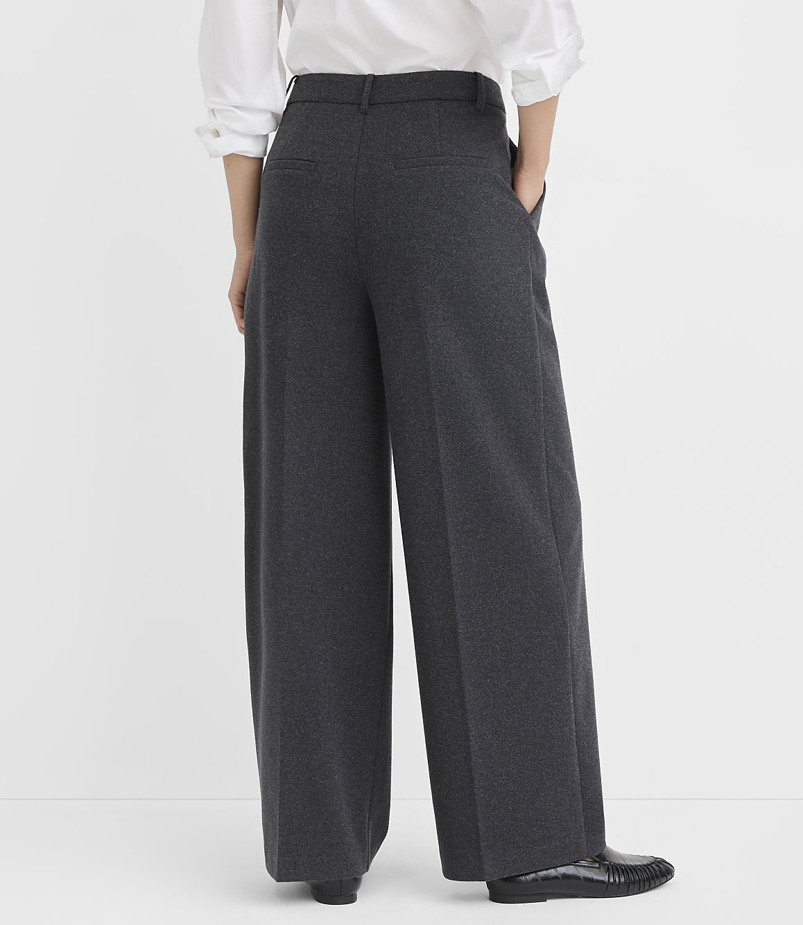 A person wearing wide-leg gray trousers and a white shirt stands against a plain white background.