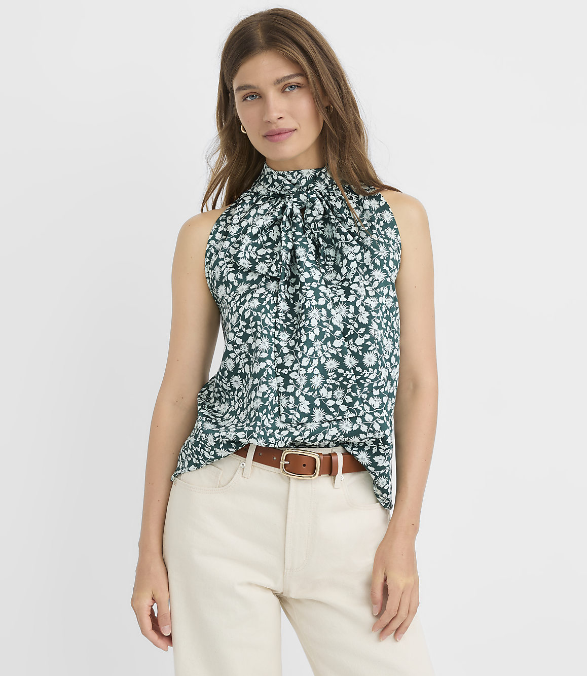 A woman in a green floral halter top and blue jeans stands against a plain white background.