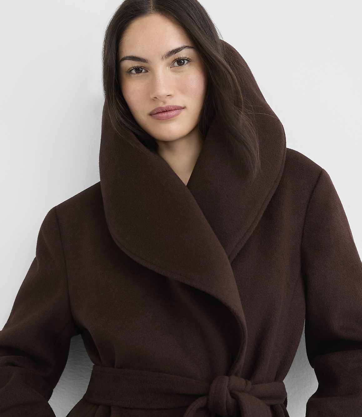 A woman in a brown coat with a large collar stands against a plain white background.