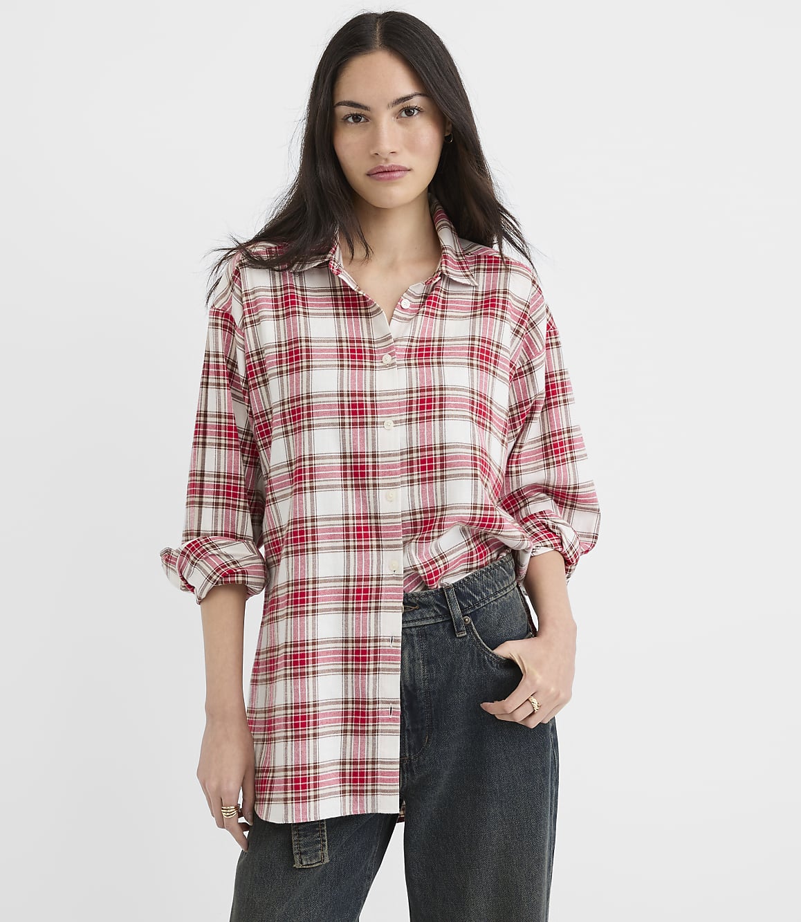 A woman in a red and white plaid shirt and dark jeans stands against a plain white background.