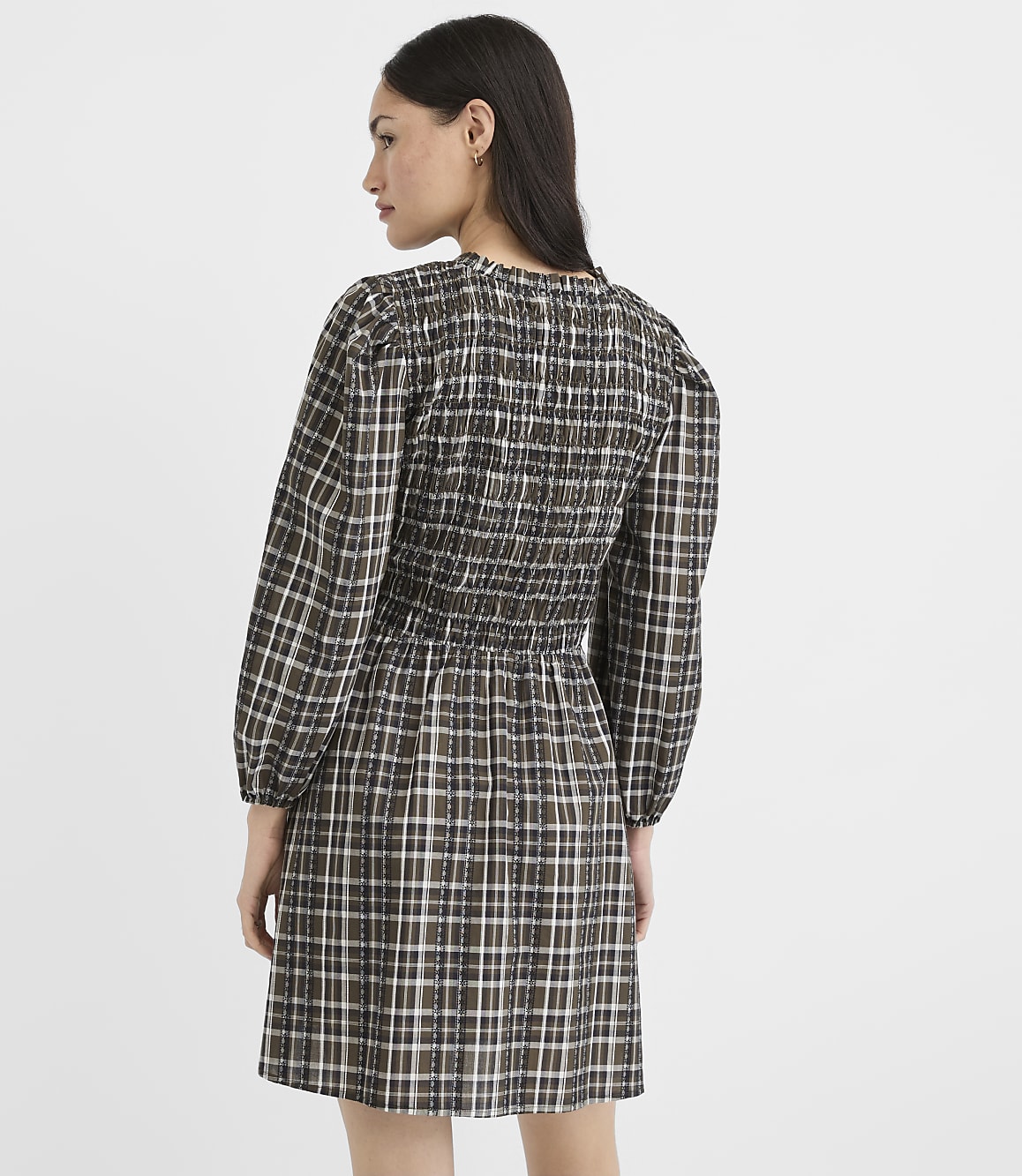 A woman in a plaid dress stands against a plain, light-colored background.