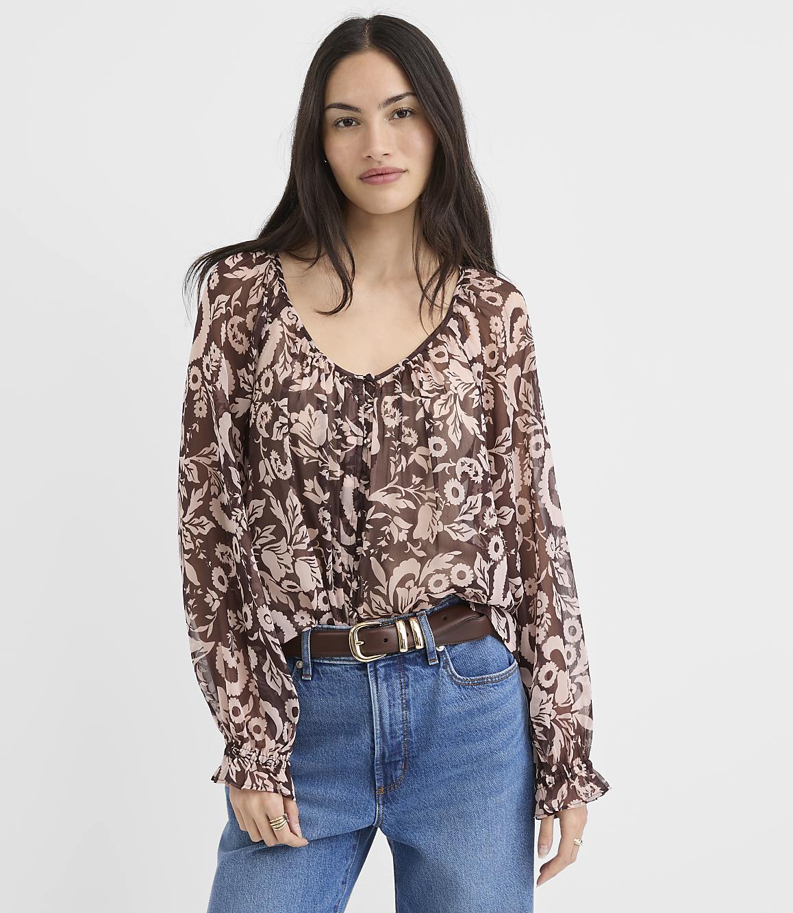 A woman in a floral print blouse and jeans stands against a plain white background.