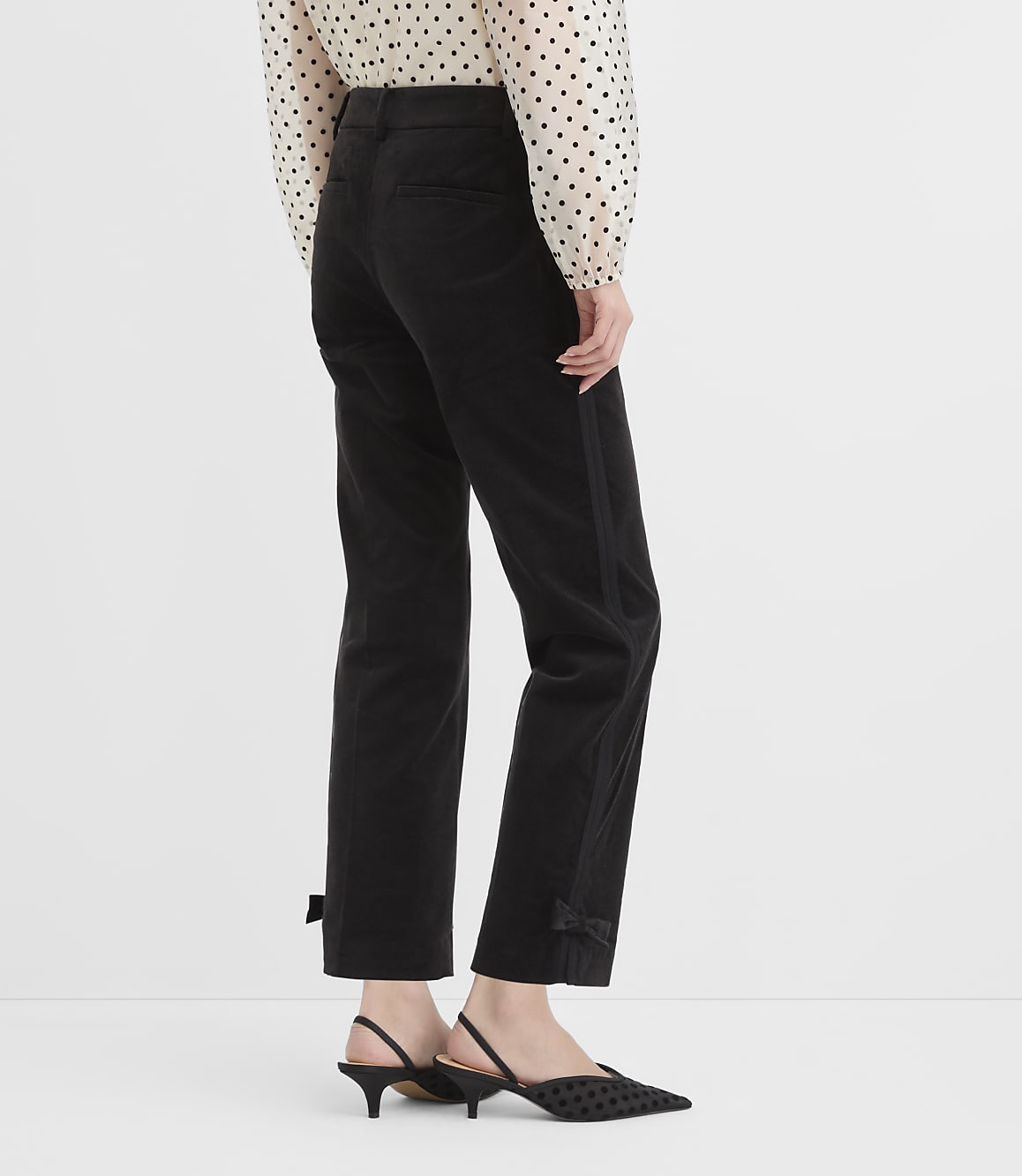 A person models black pants with bow details at the ankle and a polka-dot blouse against a plain white background.