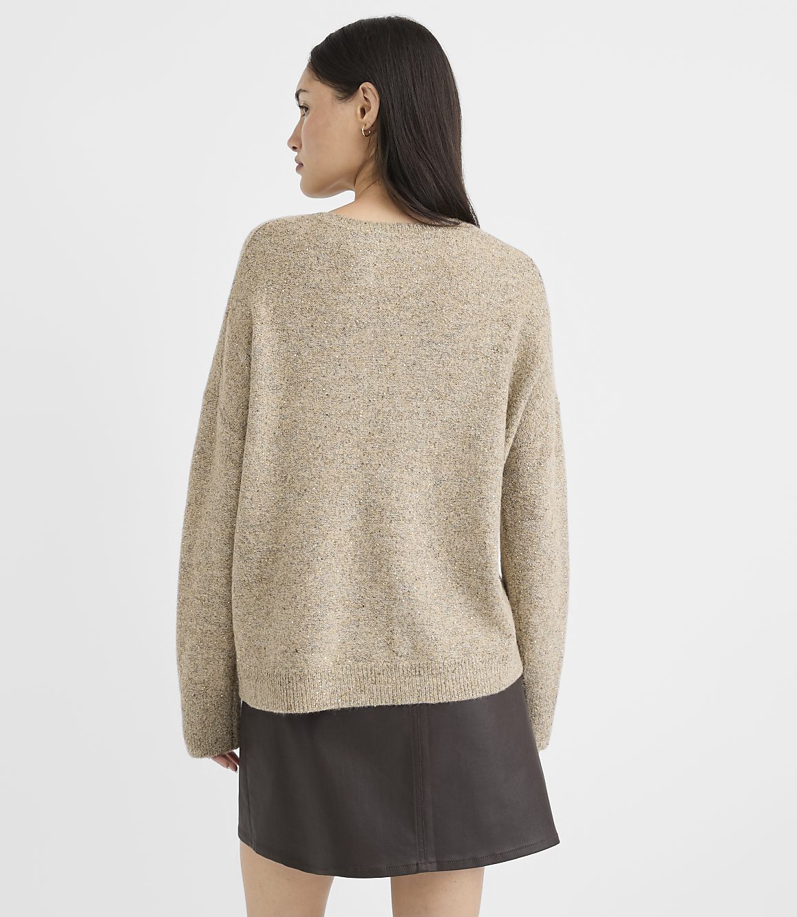 A woman in a beige speckled sweater and dark skirt stands against a plain gray background.