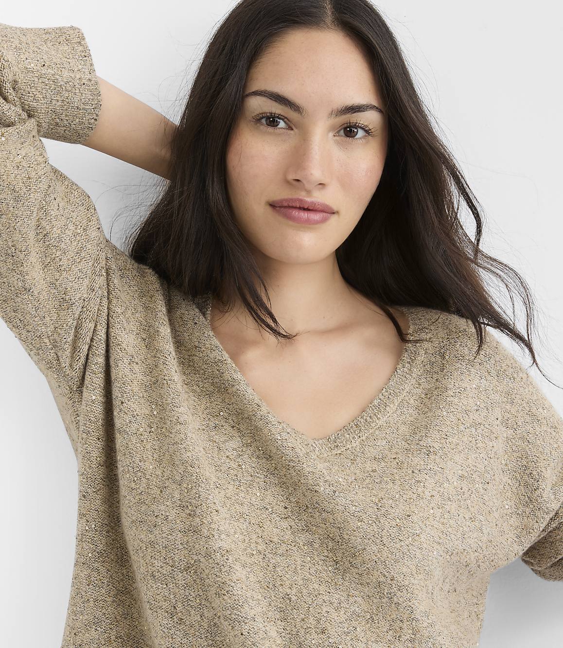 A woman with long dark hair and a v-neck sweater is in the foreground, with a plain white background.