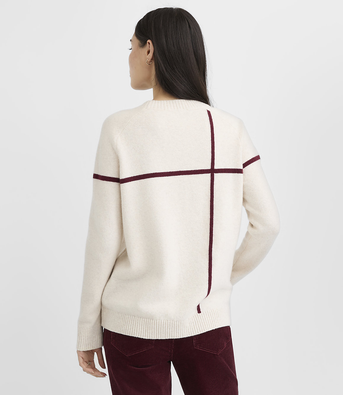 A woman in a cream-colored sweater with maroon stripes stands against a plain white background.