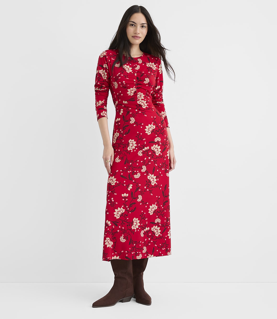 A woman in a red floral dress and brown boots stands against a plain white background.