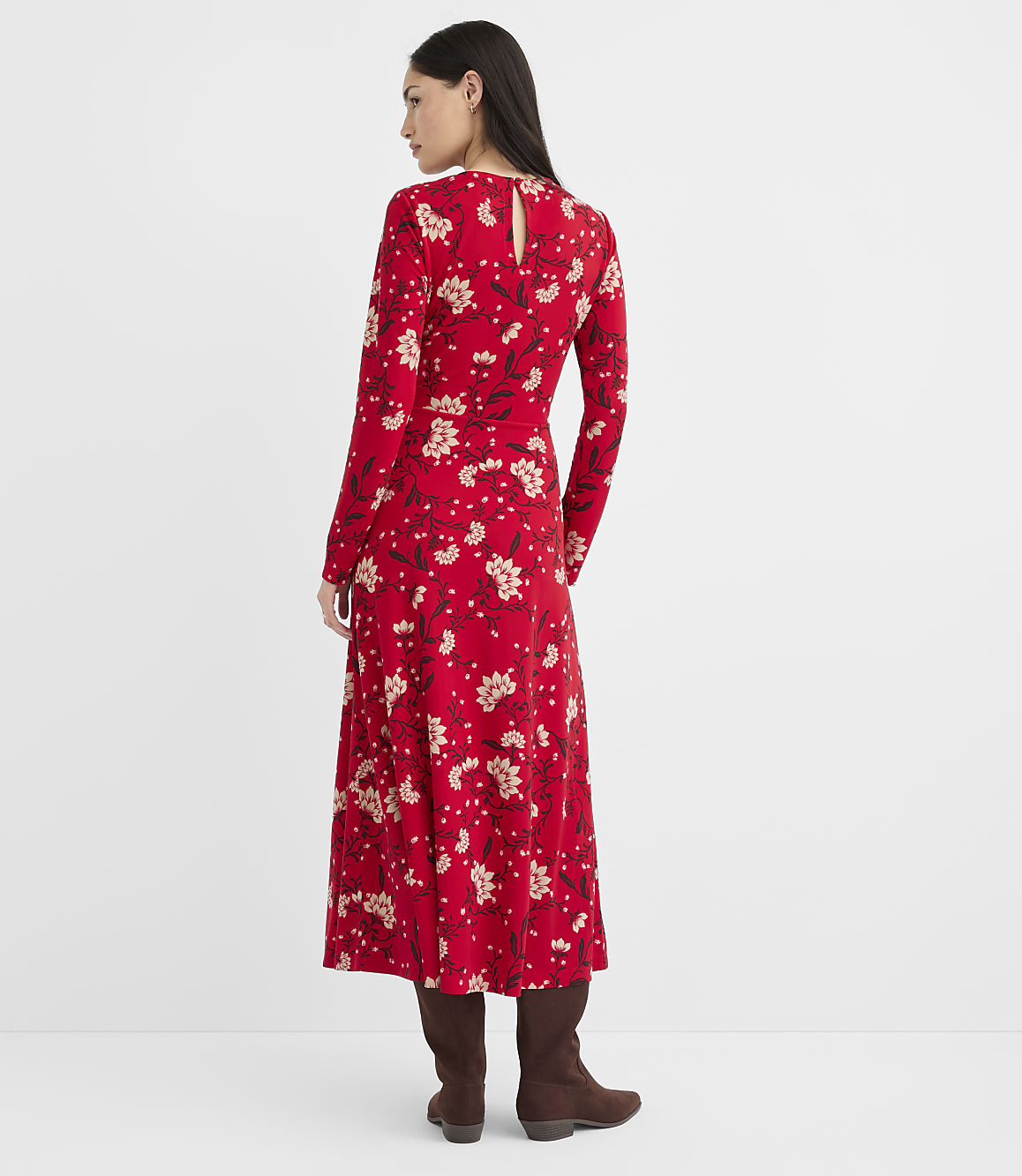 A woman in a red floral dress and brown boots stands against a plain white background.