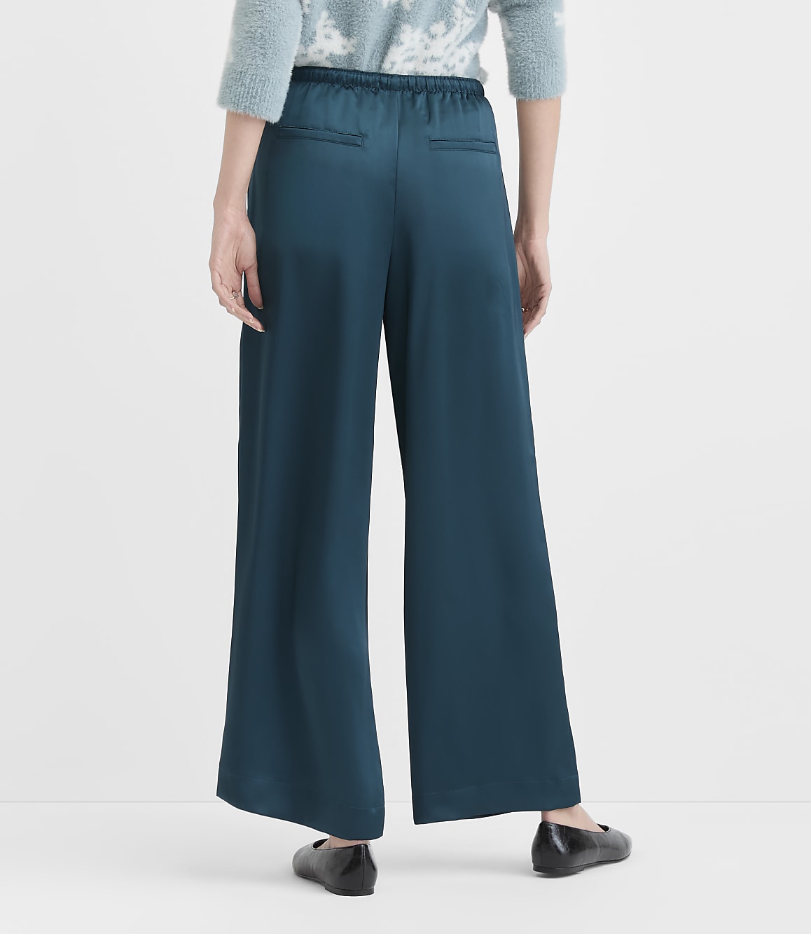 A person stands in teal wide-leg pants and black flats against a plain white background.