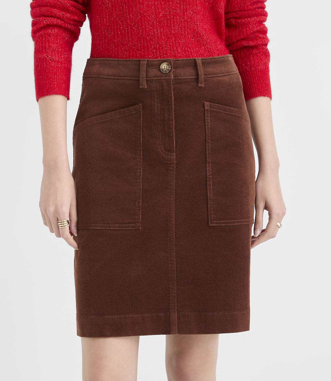 A person in a red sweater models a brown corduroy skirt with large front pockets against a plain white background.