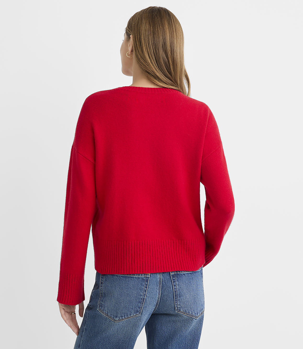 A woman in a red sweater and blue jeans stands against a plain white background.