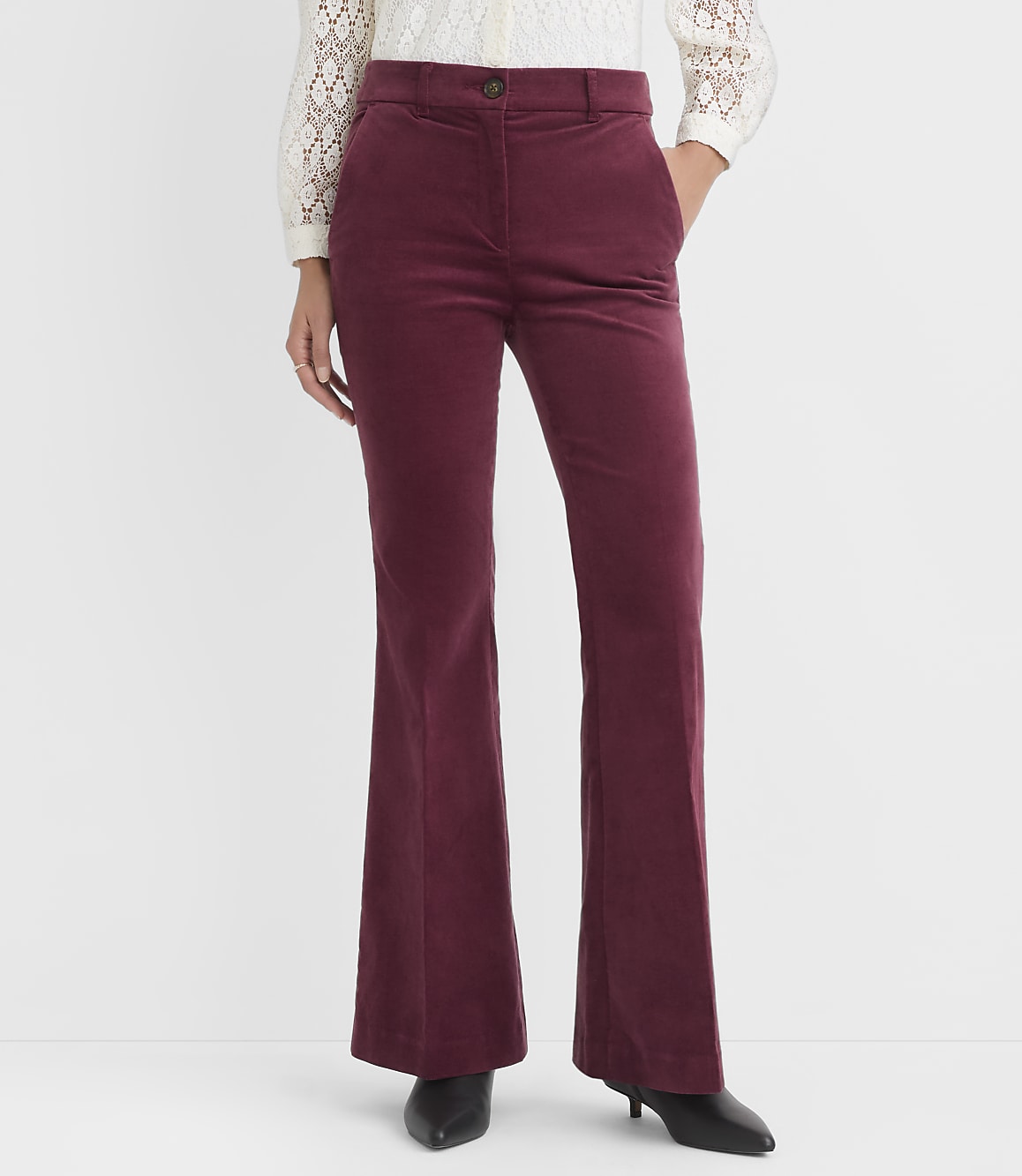 A person stands in burgundy corduroy flared pants and a white lace top against a plain white background.