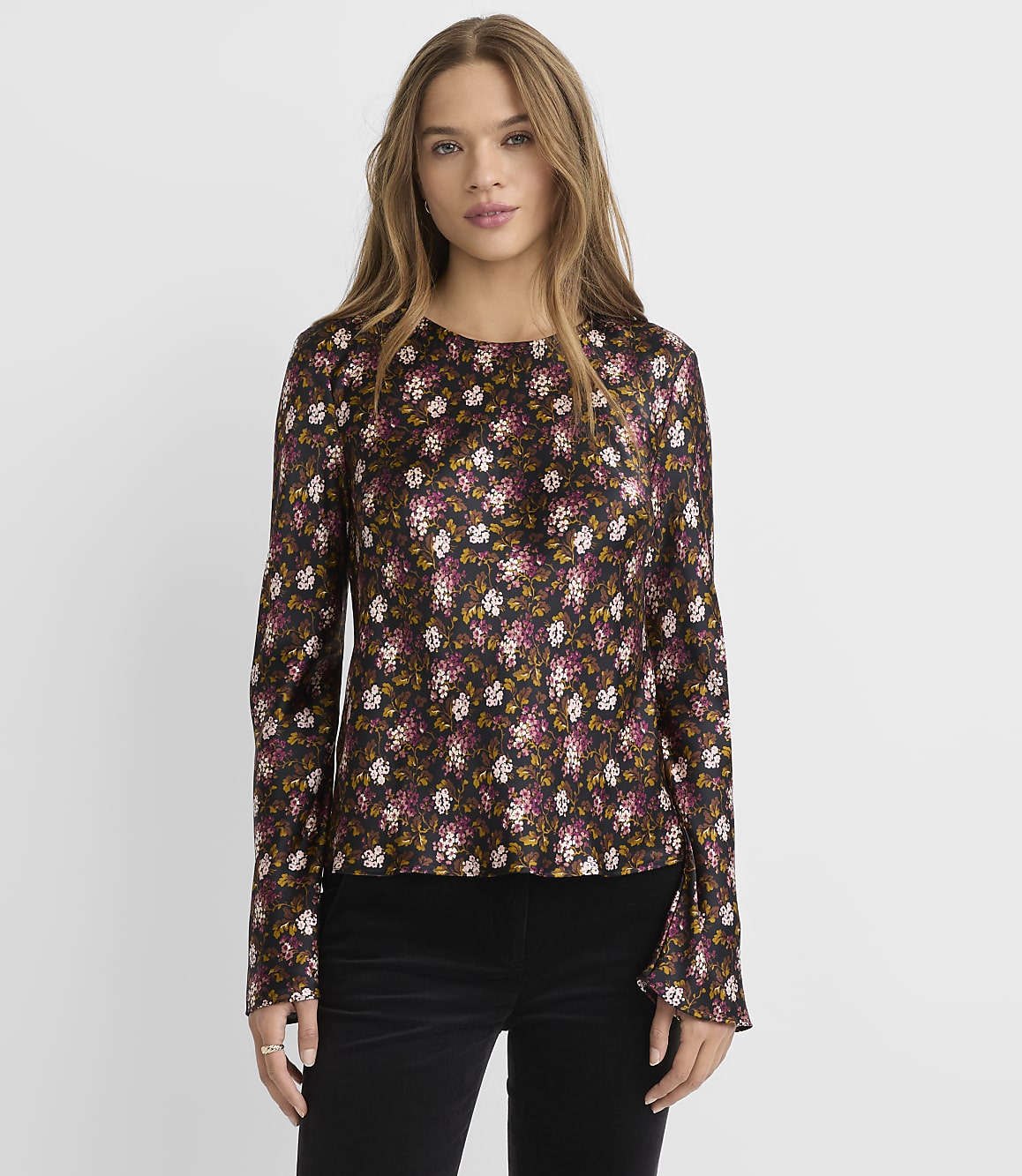 A woman in a dark floral print blouse stands against a plain gray background.