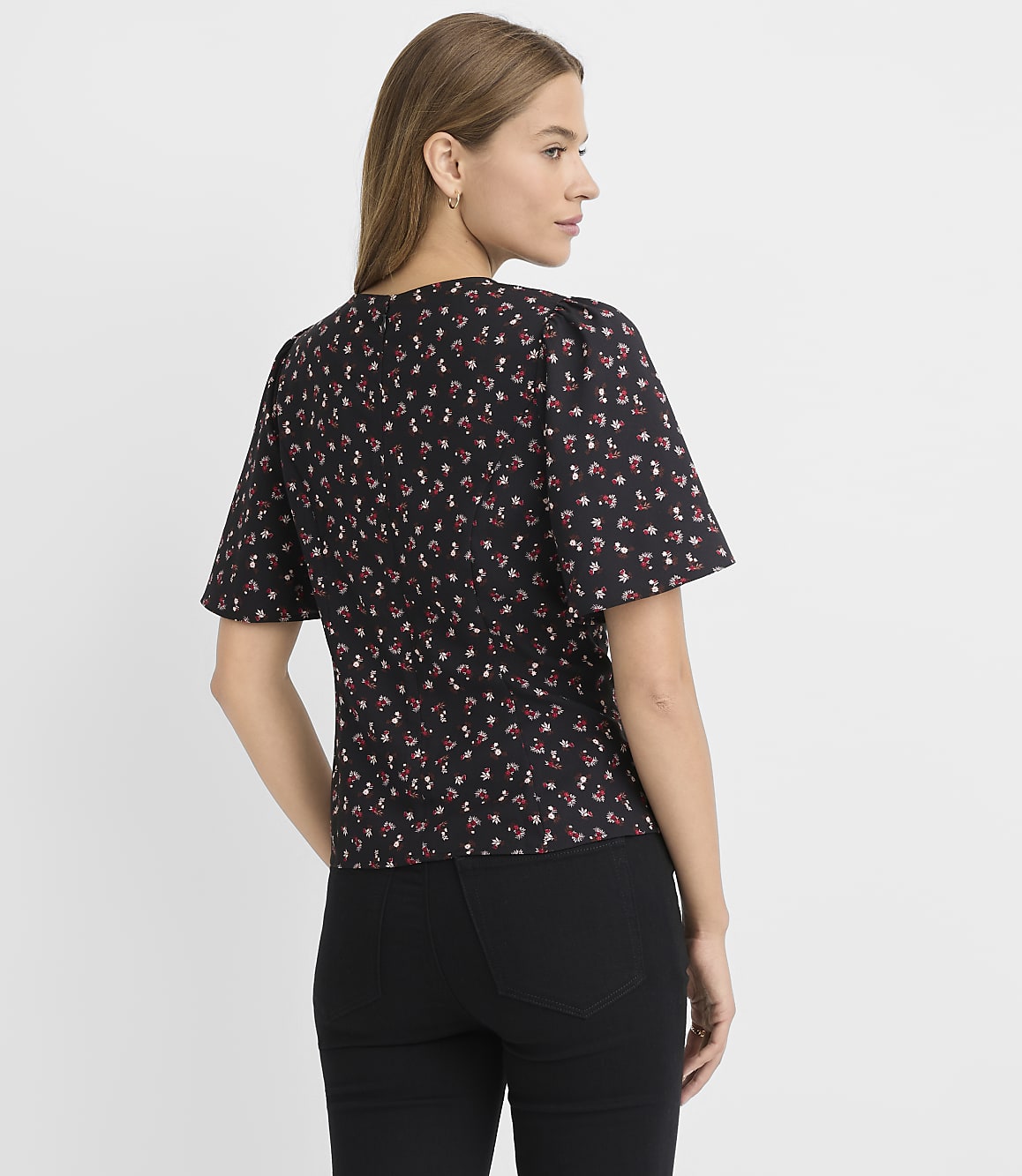 A woman in a floral print top and black pants stands against a plain white background.