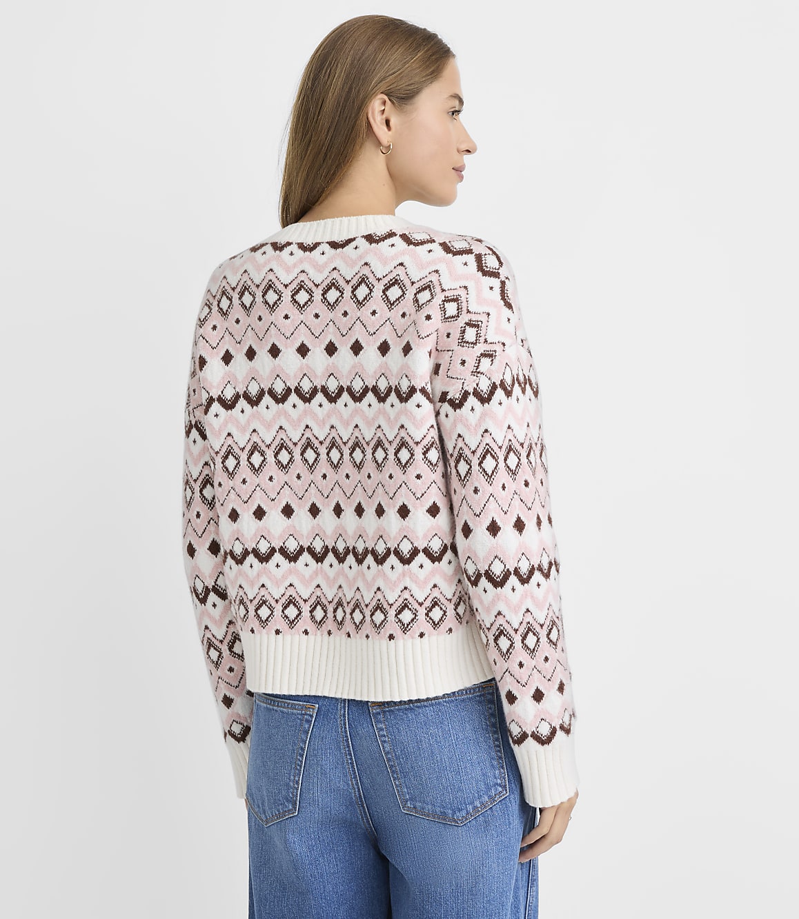 A woman in a patterned sweater and jeans stands against a plain white background.