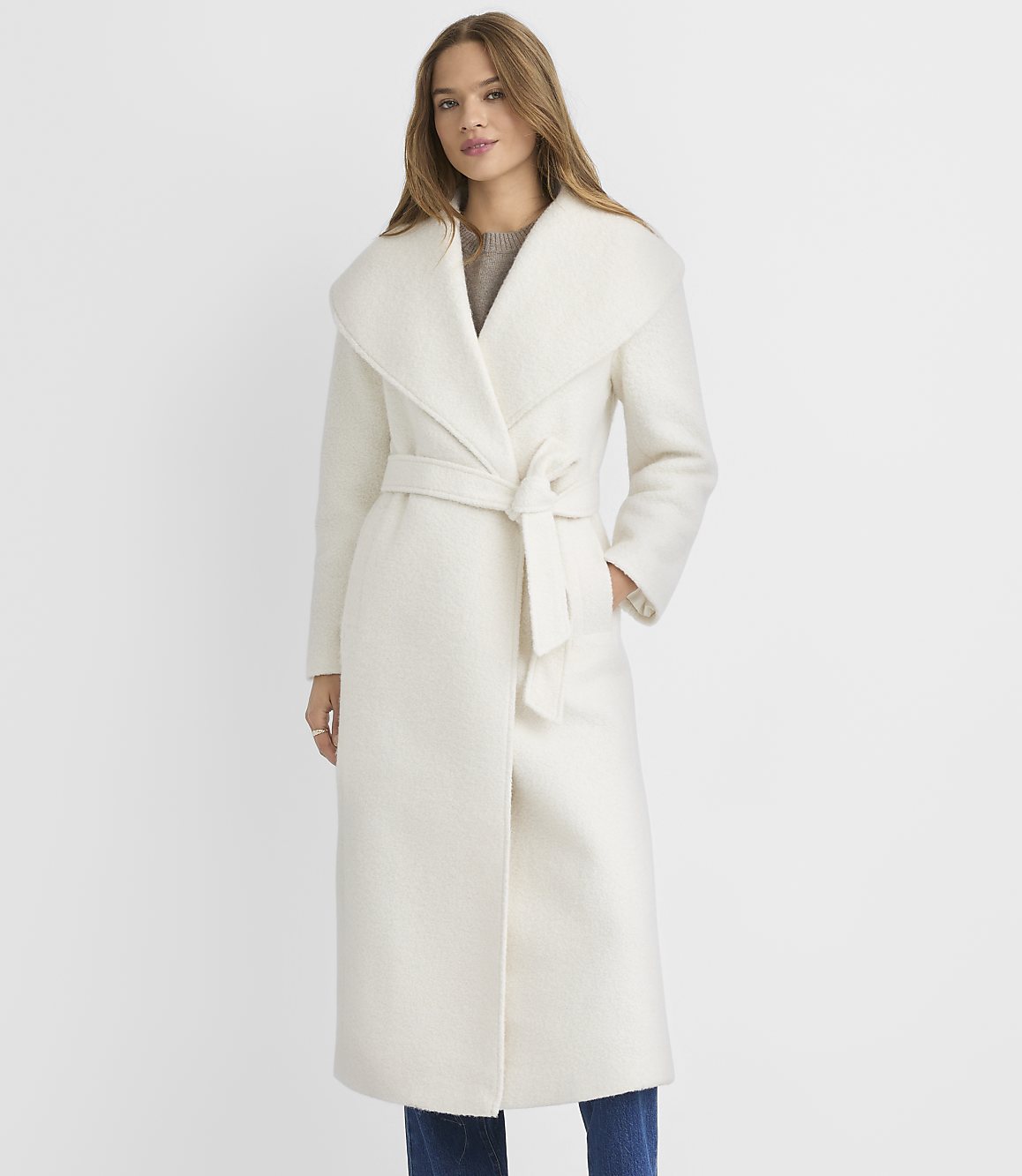 A woman in a cream-colored coat stands against a plain white background.