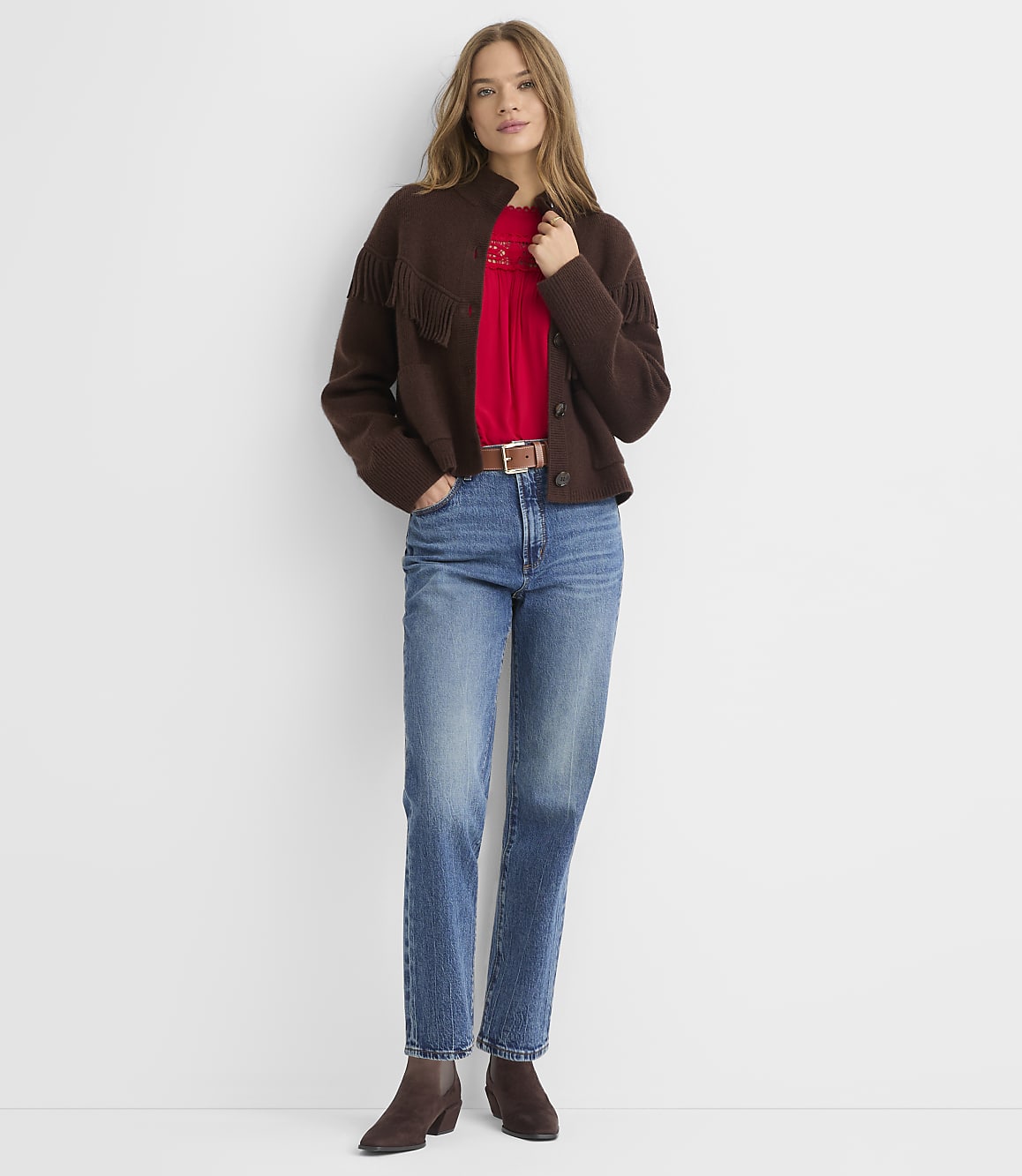 A woman in a brown cardigan and red shirt stands against a plain white background.