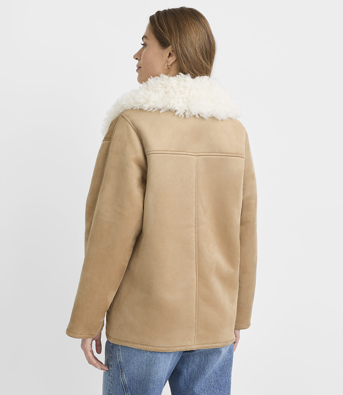 A woman in a tan suede jacket with a fluffy white collar stands against a plain white background.