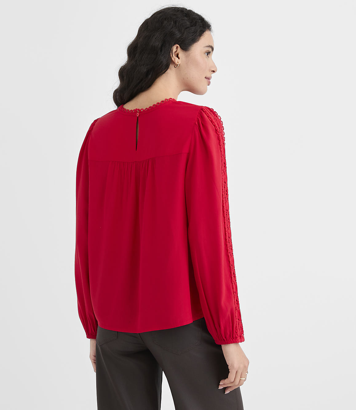 A woman in a red blouse stands against a plain gray background.