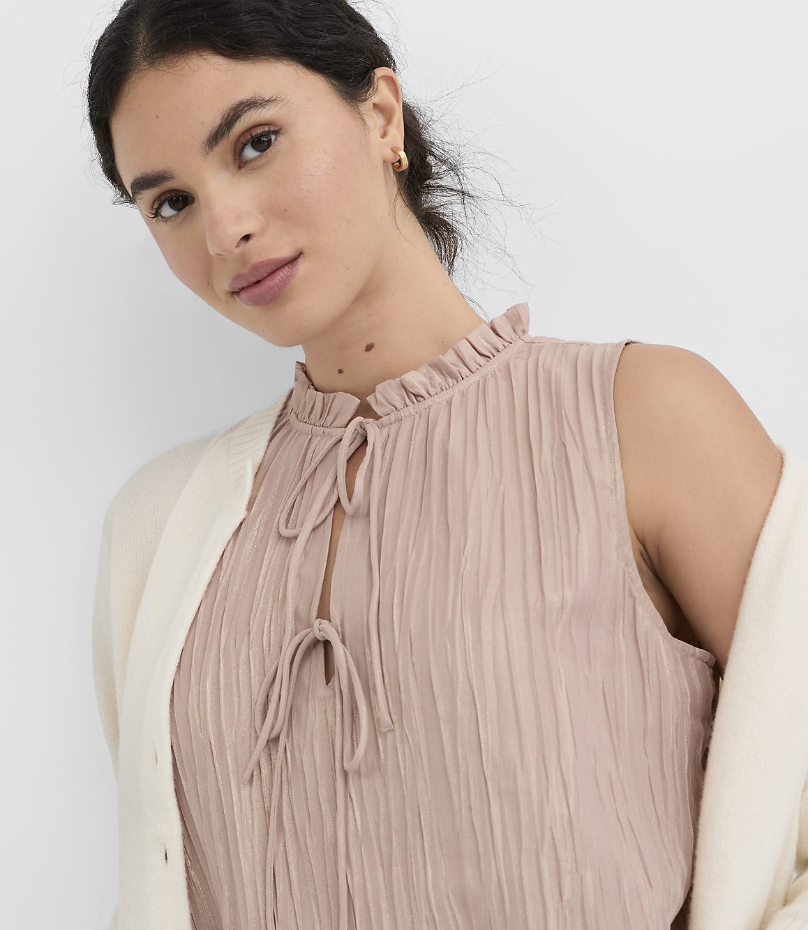 A woman in a pink ruffled top and cream cardigan is shown against a plain white background.