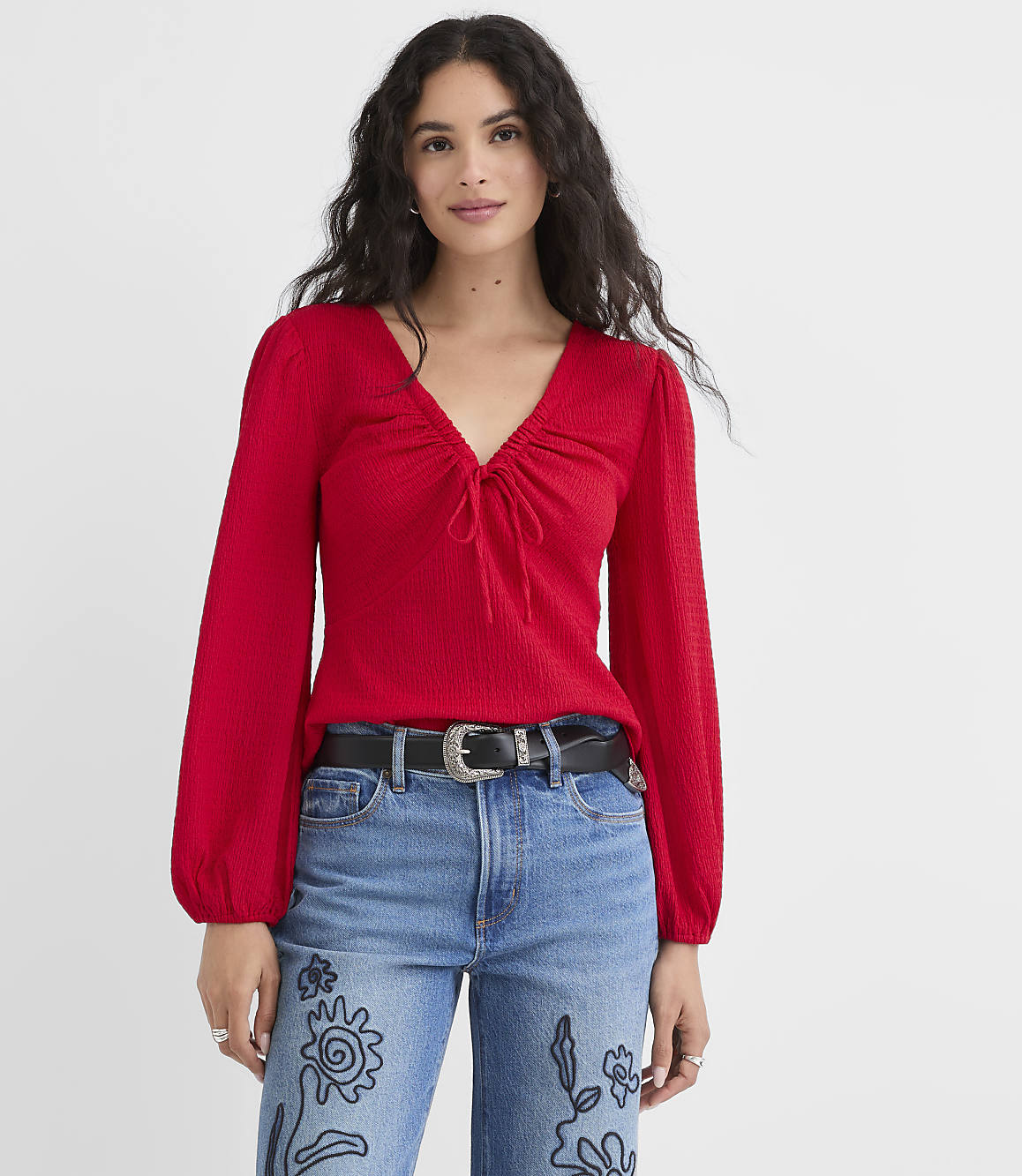 A woman in a red top and jeans stands against a plain white background.