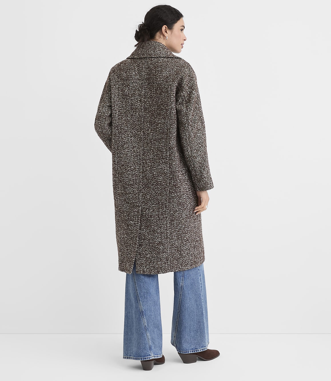 A woman in a tweed coat and wide-leg jeans stands against a plain white background.