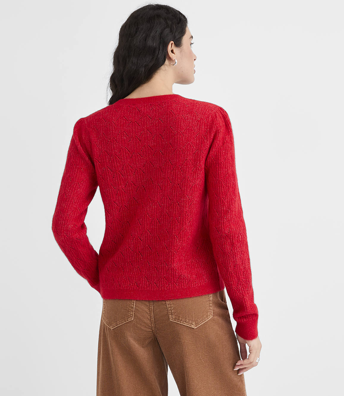 A woman in a red sweater and brown pants stands against a plain white background.