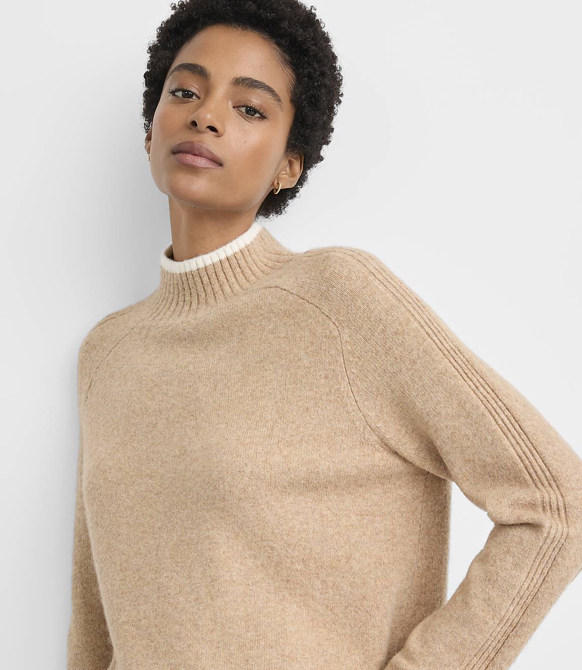 A woman in a tan mock-neck sweater is shown against a plain white background.