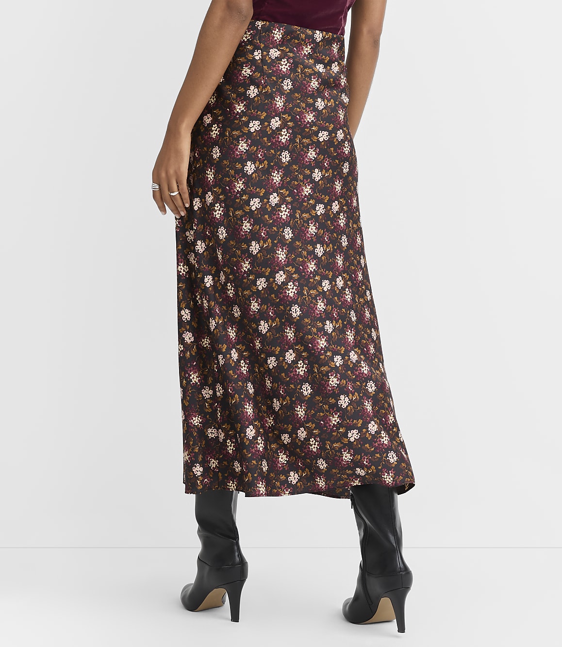 A woman in a floral print skirt and black boots stands against a plain white background.