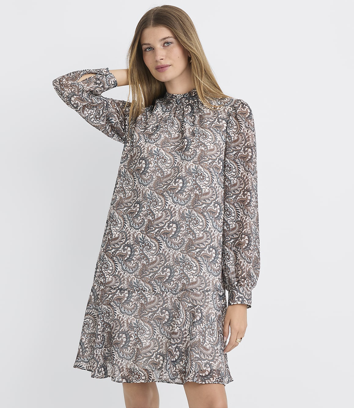 A woman in a patterned dress stands against a plain white background.