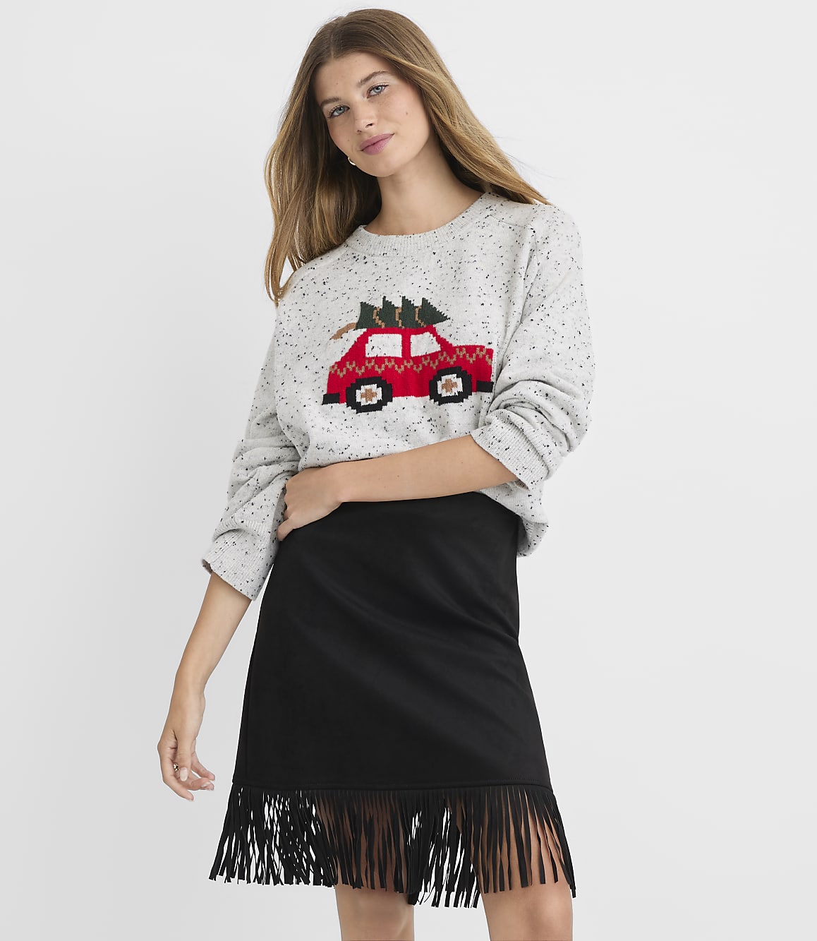A woman in a grey sweater with a red car and Christmas tree design stands in front of a plain white background.