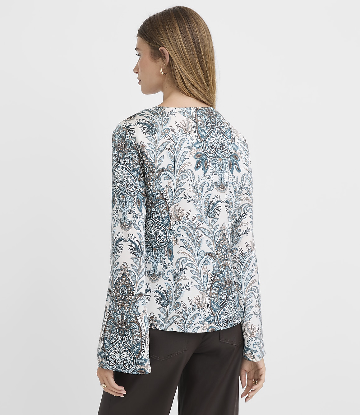 A woman in a patterned jacket stands against a plain background.