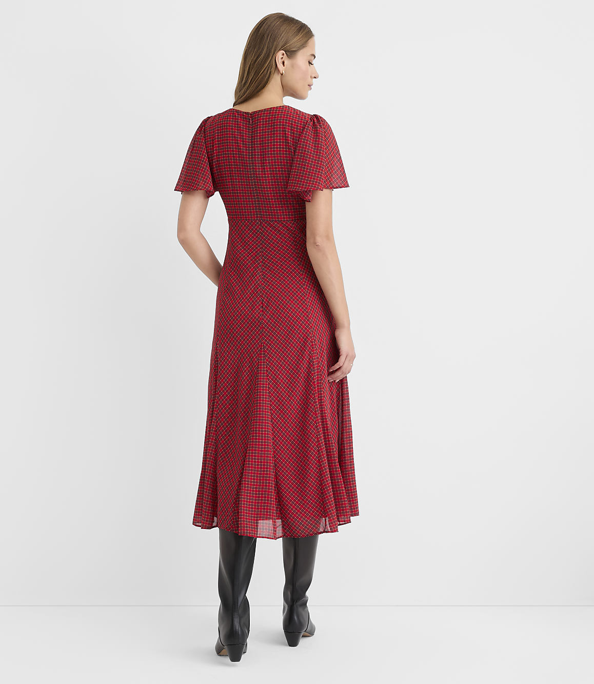 A woman in a red patterned dress and black boots stands against a plain white background.