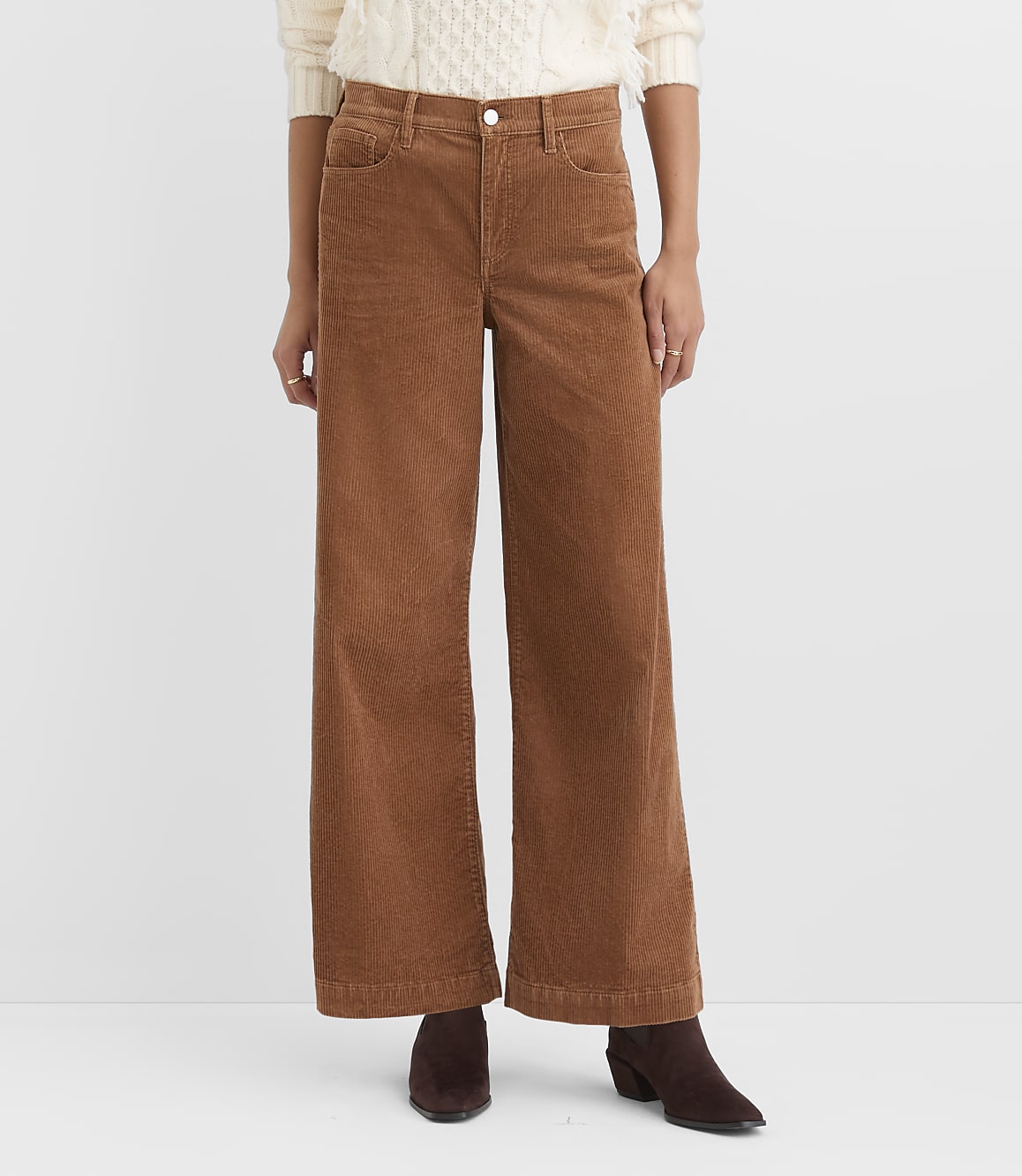 A person wearing brown corduroy pants and a cream sweater stands against a plain white background.