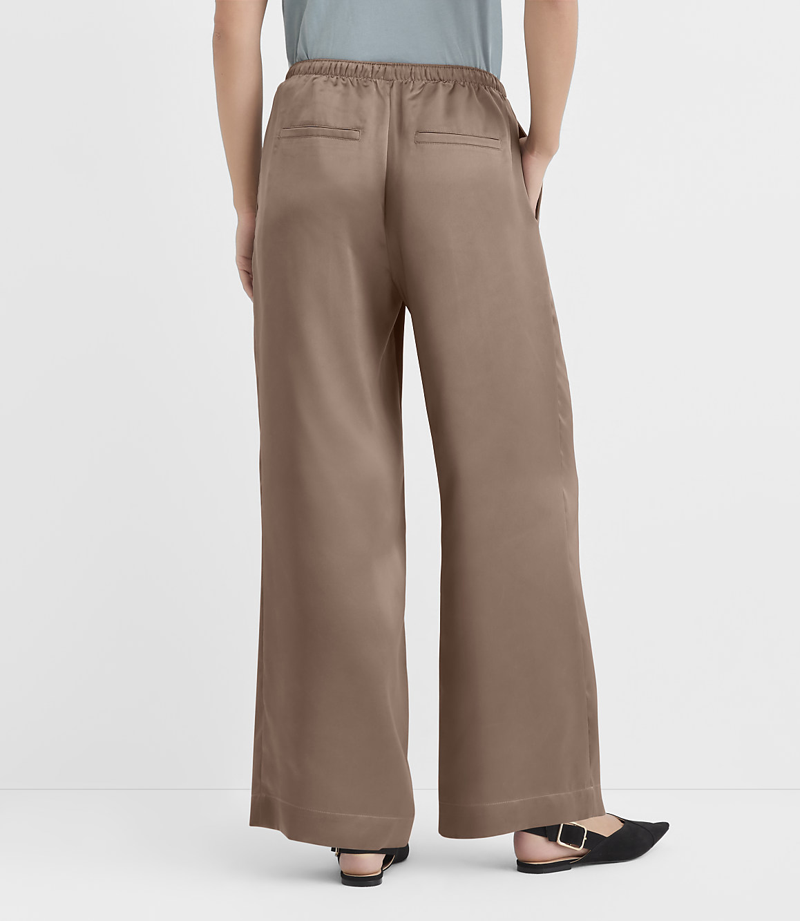 A person wearing brown wide-leg pants and black flats stands against a plain white background.