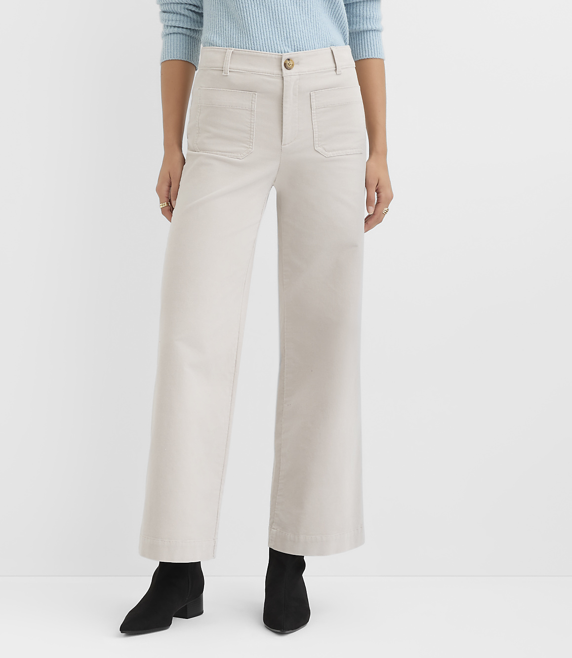 A person wearing light-colored wide-leg pants and black boots stands against a plain white background.