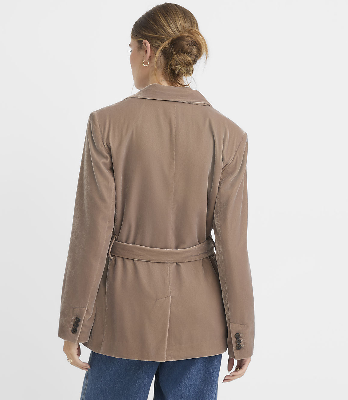 A woman in a tan velvet blazer with a belted waist stands against a plain white background.