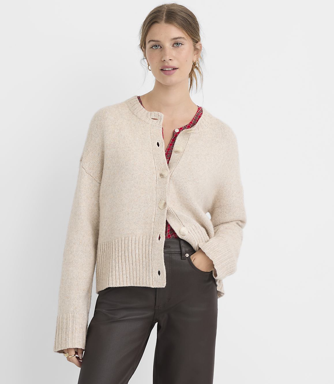 A woman in a beige cardigan and dark pants stands against a plain white background.