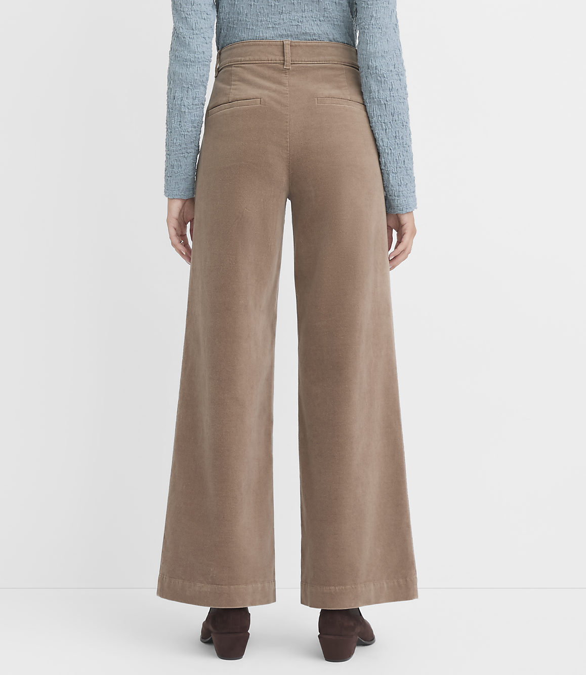 A person wearing wide-leg tan corduroy pants and a blue textured top stands against a plain white background.
